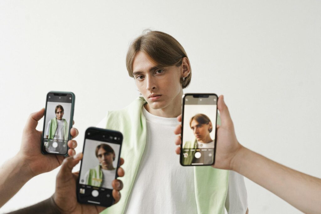 Un homme en chemise blanche est photographié avec plusieurs smartphones sur un fond uni.