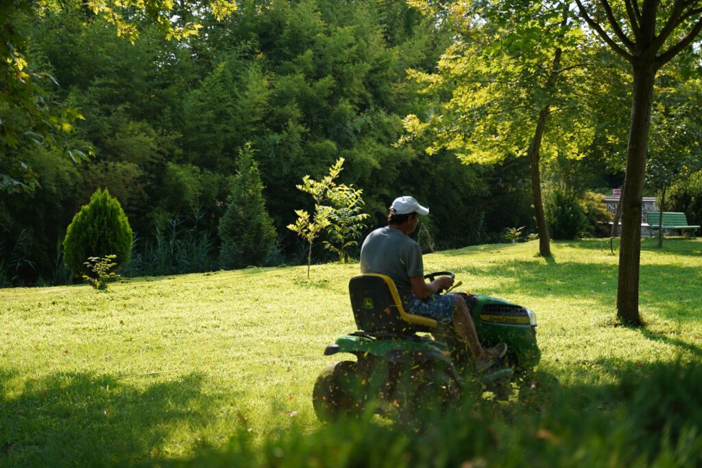 Un homme utilisant une tondeuse à gazon par une journée ensoleillée dans un jardin verdoyant, entouré d'arbres et de feuillages.