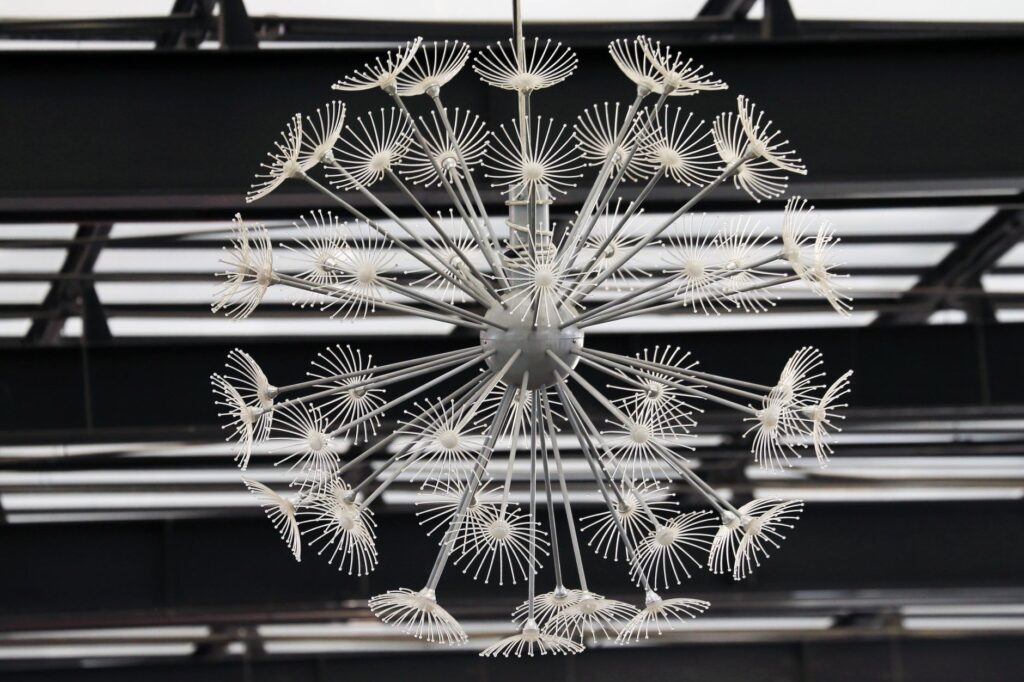 Lustre métallique moderne ressemblant à un pissenlit sur un plafond géométrique.